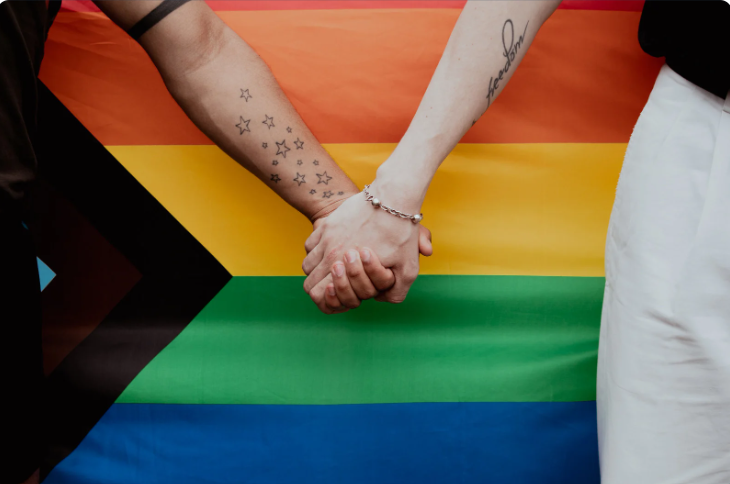 two people holding hands by a progress pride flag